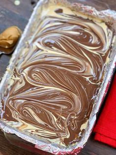 a pan filled with chocolate frosting next to a red napkin on a wooden table