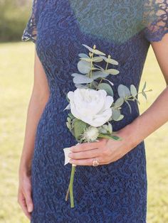 a woman in a blue dress holding a white rose and greenery boutonniere