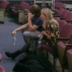 two people are sitting in the middle of an auditorium with empty seats and one is holding a water bottle