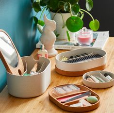 a wooden table topped with containers filled with makeup and other items next to a potted plant