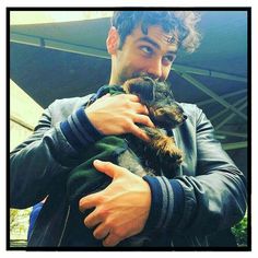 a man holding a small dog in his right hand and looking at the camera while wearing a leather jacket