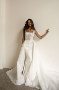 a woman in a white wedding dress leaning against a wall with her arms spread out