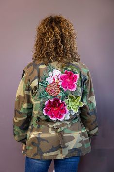 a woman in camouflage jacket with flowers on it's back and long curly hair