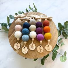 six wooden keychains with different colored pom poms hanging from them on a wood plate