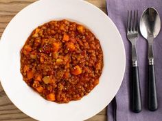 a white plate topped with lentils and carrots next to a fork, knife and spoon