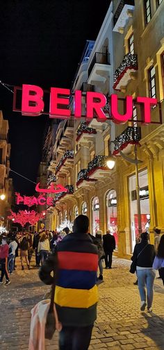 people are walking down the street in front of buildings with lights and signs on them