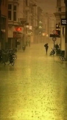 a city street is flooded with water and people are walking down the sidewalk in the rain