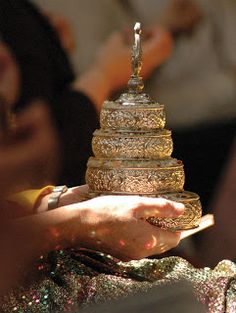 a person holding a large stack of gold jewelry in their hands with other people behind them