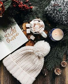 a white knitted hat sitting on top of a wooden table next to a candle