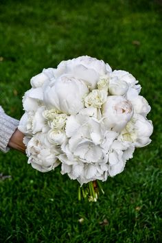 a bouquet of white flowers in someone's hand on some green grass and grass