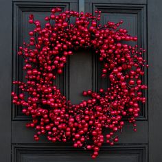 a christmas wreath on the front door of a house with red baubles hanging from it