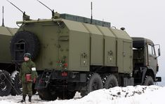 a man standing in front of an army truck on the snow covered ground with two other trucks behind him