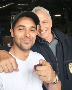 two men posing for a photo in a garage with one pointing at the camera and smiling