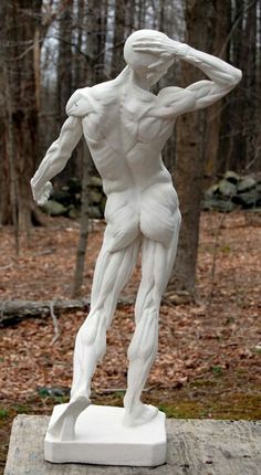 a white statue of a man standing on a wooden platform in the woods with his hands behind his head