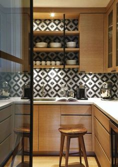 a kitchen with wooden cabinets and black and white tile backsplash, counter tops, and stools