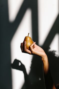 a person holding an apple in their hand with shadow on the wall behind them,