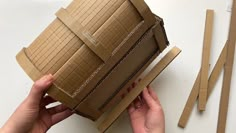 someone is holding an open cardboard box with strips of brown paper next to it on a white surface