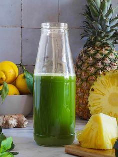 a green smoothie in a glass pitcher next to sliced pineapple