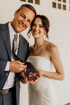 a man in a suit and tie holding a small object next to a woman in a white dress