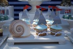 cupcakes with blue frosting and sailboats on them are sitting on a table