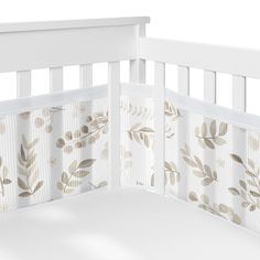 a white crib with leaves on it and the top rail is closed to show the bedding