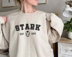 a woman standing in front of a bed wearing a sweatshirt that says stark est 1910