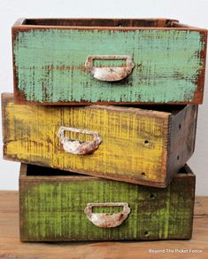 three green and yellow drawers sitting on top of a wooden table in front of a white wall