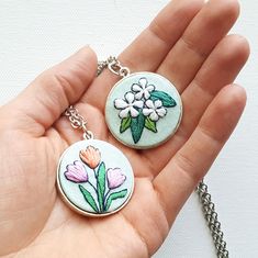 two flowers are on the back of this keychain and one is being held by someone's hand