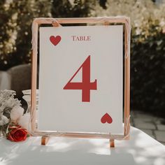 a table number sign sitting on top of a white cloth covered table with red hearts