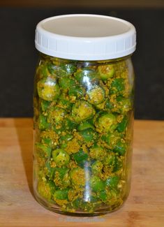 a glass jar filled with green peppers on top of a wooden table