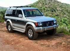 a silver four door suv parked on top of a dirt road next to a lush green hillside