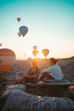 two people sitting on top of a bed next to hot air balloons