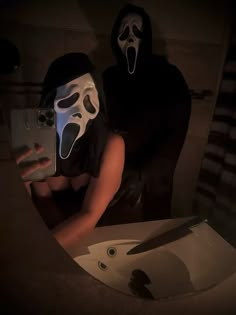 two people with masks on taking a selfie in front of a mirror while holding a cell phone