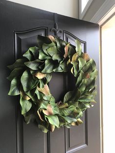 a wreath is hanging on the front door with green leaves and brown trim around it