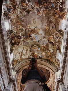 a person taking a photo in front of a ceiling with many paintings on the walls