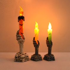 three lit candles in the shape of hands with rocks and stones around them on a table