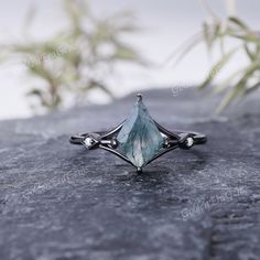 a ring with an aqua green stone on it sitting on top of a black rock