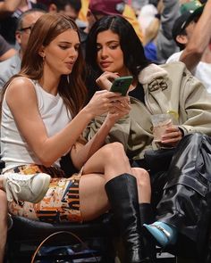 two women sitting next to each other in front of a crowd looking at a cell phone