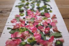 pink and green flowers are scattered on a white table runner that sits on a wooden floor