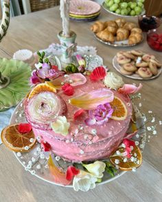 a pink cake with flowers and oranges on it sitting on a table next to other desserts