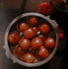 a bowl filled with lots of brown balls on top of a wooden table next to a red flower