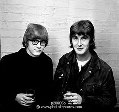 two young men standing next to each other holding glasses in front of a brick wall