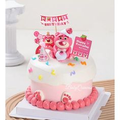 a birthday cake decorated with pink and white frosting, teddy bears on the top