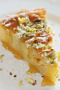 a piece of pie on a white plate covered in powdered sugar and pistachio