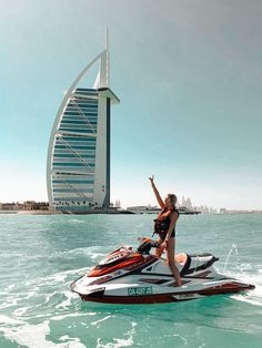 a woman riding on top of a jet ski in the ocean next to a tall building