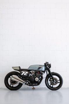 a black motorcycle parked next to a white brick wall in a room with concrete flooring