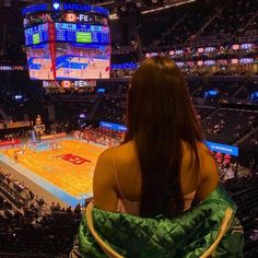 a woman sitting in a chair watching a basketball game on the big screen at an arena