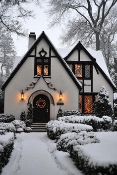 Snow-covered Tudor house with glowing windows. The charming fusion of history and contemporary flair in modern Tudor houses can transform your living space from “just nice” to “royalty-approved.” Tudor House Colors Exterior, Tudor Cottage Living Room, Storybook Tudor Cottage, Tudor Gingerbread House, Tudor Style House Exterior, French Hood Tudor, Gothic Tudor House, Sims 4 Tudor House