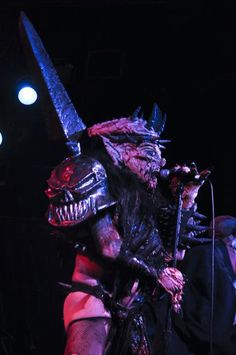 a man dressed as an alien holding a microphone in front of two other men on stage