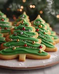 christmas cookies decorated with green icing and gold decorations on a plate next to a tree